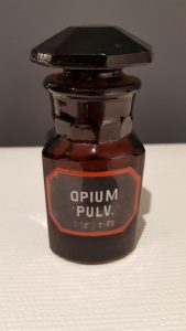 Szklane naczynie aptekarskie (sztanda) zawierające sproszkowane opium, które przez wieki stosowano jako środek przeciwbólowy, nasenny, uspokajający i odurzający.